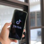 Hand holding a smartphone displaying the TikTok app, representing the social ad click that starts the conversion path.