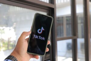 Hand holding a smartphone displaying the TikTok app, representing the social ad click that starts the conversion path.